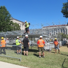 A team of workers places platform pieces on the media riser structure.