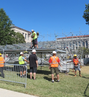 A team of workers places platform pieces on the media riser structure.