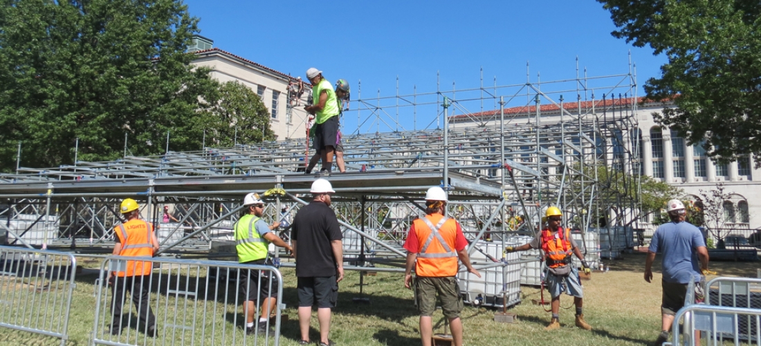 A team of workers places platform pieces on the media riser structure.