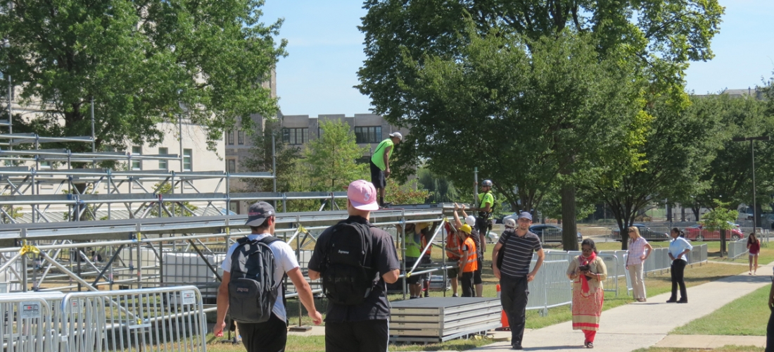 Students walk through fencing on the University Mall past the media riser under construction.